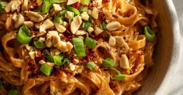 Delicious bowl of spicy peanut butter noodles garnished with fresh herbs